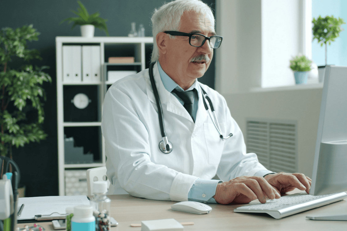 an elder doctor typing on computer - Why Should AI Be Part of Healthcare Workflows? Explained