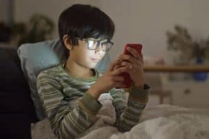 boy with eyeglasses using a smartphone in bed 300x200 - boy with eyeglasses using a smartphone in bed
