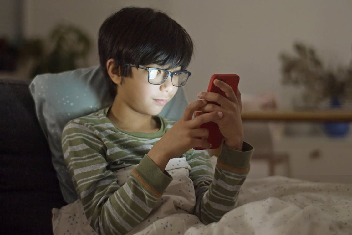 boy with eyeglasses using a smartphone in bed - Home