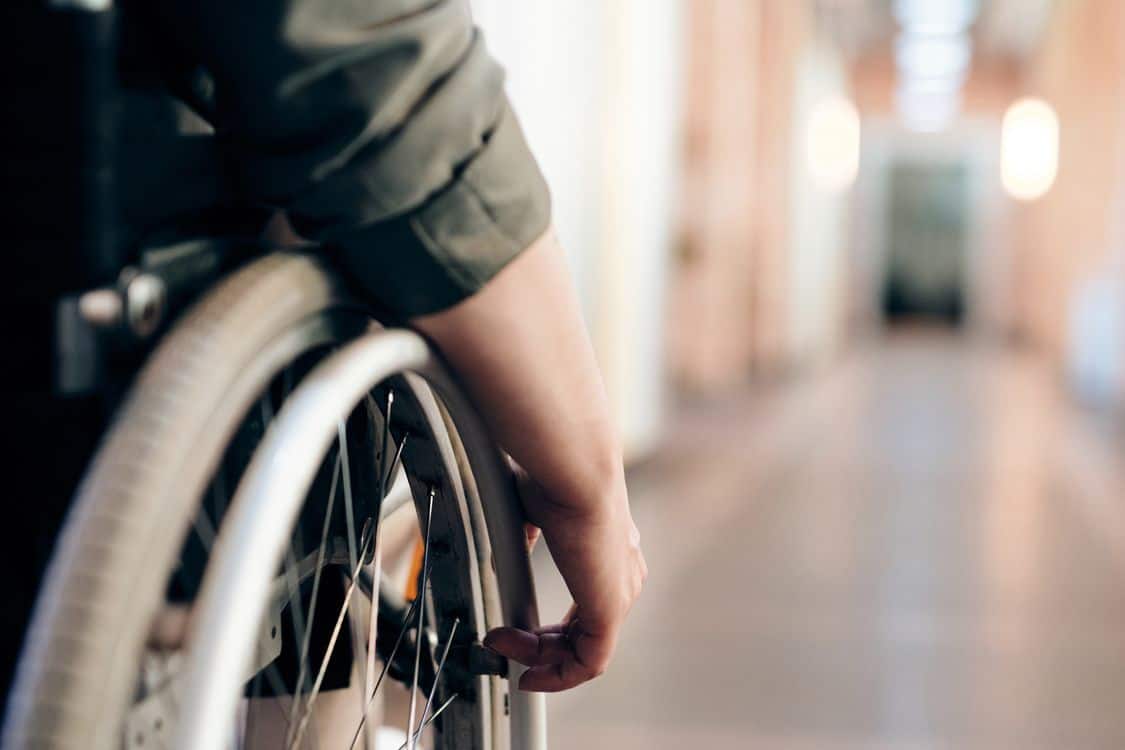 close up of a person in a wheelchair is navigating an indoor hallway - SSA Says Its Disability Backlog Is Shrinking. Arizona Applicants Tell a Different Story