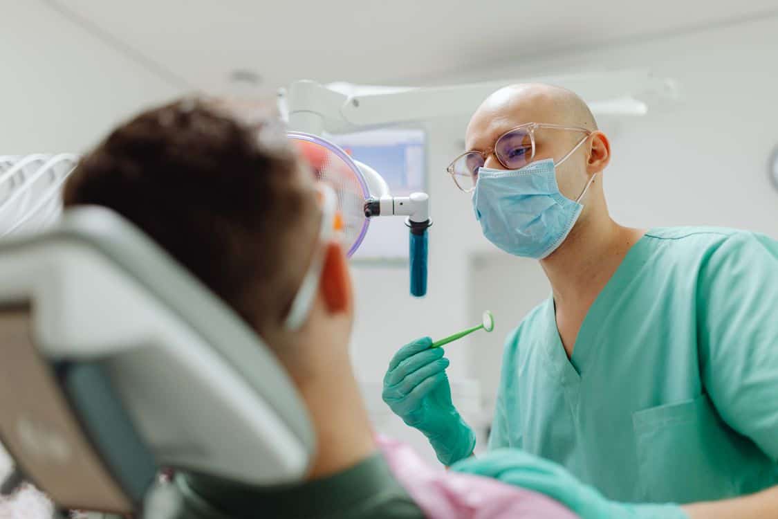 Dentist examining a patients teeth with - Home